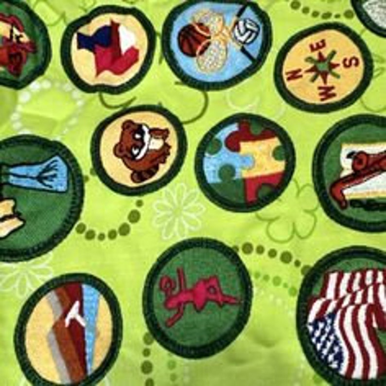 Puede incluir: Tela verde con un patr&oacute;n repetido de c&iacute;rculos blancos y tr&eacute;boles verdes. La tela est&aacute; cubierta con varios parches bordados de colores, incluyendo una br&uacute;jula, un bal&oacute;n de baloncesto, una abeja, una mariposa, un mapache, una monta&ntilde;a, una bota, una bandera y una ni&ntilde;a haciendo gimnasia.