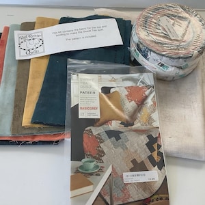 以下が含まれることがあります： 様々な色の生地が入ったキルトキット。ティール、コーラル、ゴールドなど。キットにはパターンと生地のロールが含まれています。「Red Rooster Quilts」のロゴと「Sweet Tea Quilt」の文字が見えます。