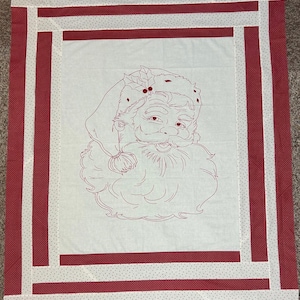 May include: A festive Christmas quilt with a red outline of Santa Claus on a white background. The quilt is framed with red and white striped borders, creating a holiday design. The quilt's dimensions are approximately 100 cm x 100 cm.