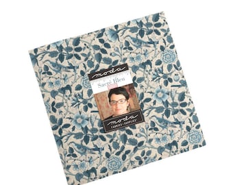 May include: A square fabric piece with a floral and bird pattern in shades of blue and cream. A label with the text "Sacré Bleu" and a woman's image is on top. The fabric is from Moda Fabrics + Supplies.