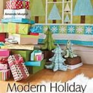 Puede incluir: Un libro titulado "Modern Holiday: Deck the Halls with 18 Sewing Projects" que presenta una pila colorida de regalos envueltos, una colcha de árbol de Navidad y un adorno de árbol de Navidad verde y azul.