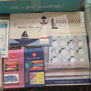 May include: A quilting kit with various supplies. Includes a "Sailaway Quilt Pattern", fabric, a "Half Rectangle Trimmer", and heat-resistant pins. The finished quilt size is 36.5" x 36.5". The kit is themed around a nautical theme.