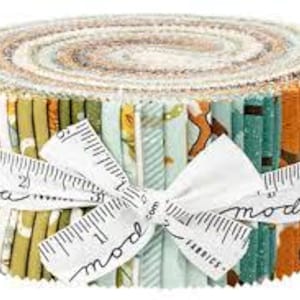 May include: A fabric roll featuring a variety of patterned fabrics in shades of green, orange, and cream, secured with a white ribbon printed with a ruler design and the word "moda". The roll is tightly wound, showcasing the different fabric patterns.