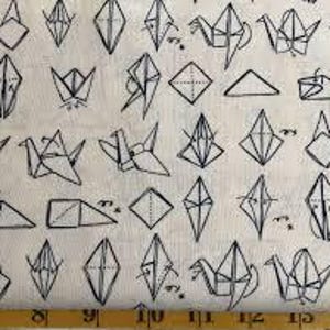 May include: Off-white fabric with a repeating pattern of black origami cranes and geometric shapes. The design includes various folded paper figures, creating a textured and artistic appearance. A yellow ruler is at the bottom.