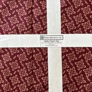 May include: A pack of 12-inch quilt squares featuring a red fabric with a white floral pattern. The fabric is labeled "Idaho Prairie Wheat" by Henry Glass & Co. Inc.