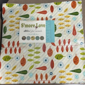 Puede incluir: Un paquete de tela con un patrón repetido de hojas estilizadas en tonos verdes, naranjas y amarillos sobre un fondo crema. La tela está etiquetada como "S'more Love" por Eric & Julie Comstock.