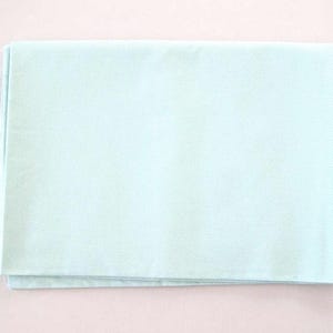 May include: A folded, light blue fabric with a subtle dotted texture. The fabric is rectangular and appears to be made of a soft material. The edges of the fabric are slightly frayed. The overall color is a pale, muted blue.
