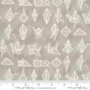 May include: Gray fabric with a white origami crane and geometric shapes pattern. The fabric has a ruler printed along the bottom edge, with measurements in inches. The fabric is from Moda.