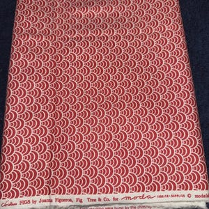 Op de afbeelding: Een gevouwen stof met een herhalend rood en wit sint-jakobsschelpenpatroon. De stof is gelabeld met "Christmas FIGS by Joanta Figueroa, Fig Tree & Co. for moda FABRICS SUPPLIES". De tekst "and the stocking were hung by the chimney" is ook zichtbaar.