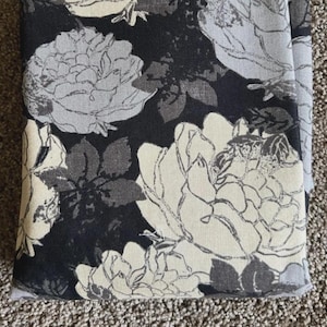 Pode incluir: Um artigo de tecido com um padrão floral. O design apresenta grandes flores estilizadas em tons de branco, cinza e preto sobre um fundo escuro. As flores têm contornos detalhados, criando uma aparência texturizada.