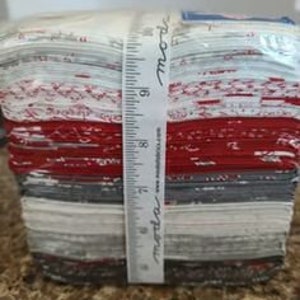 Puede incluir: Una pila de cuadrados de tela en rojo, blanco y gris con un patrón floral blanco y gris. La tela está empaquetada y lista para ser utilizada para acolchar u otras manualidades.