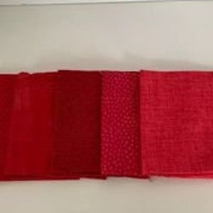 Op de afbeelding: Vier rode vierkante stoffen, elk met een andere textuur. De vierkanten zijn in een rij van links naar rechts gerangschikt, met de gladde textuur links en de ruwe textuur rechts.