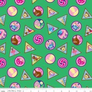 May include: Green fabric with a repeating pattern of colorful circles and triangles. The circles feature various Disney characters and icons, including Mickey Mouse, Cinderella's castle, and a guitar. The triangles are solid pink.