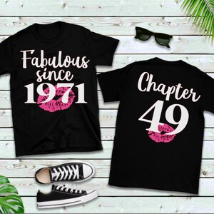 May include: Two black t-shirts with white text. The first shirt says "Fabulous since 1971" with a pink lip print. The second shirt says "Chapter 49" with a pink lip print.