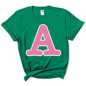 May include: A green t-shirt with a pink letter A on the front. The letter is outlined in white and has a rounded, bubbly style.