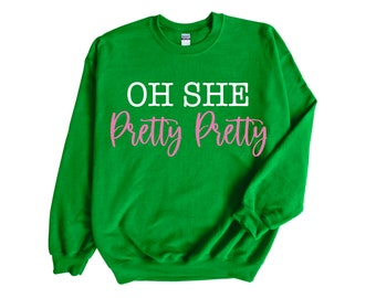 May include: Green sweatshirt with the text "OH SHE Pretty Pretty" in white and pink lettering.