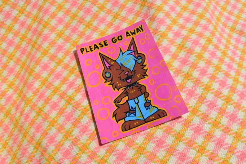 May include: A pink and orange sticker with a cartoon wolf wearing blue jeans and a black choker. The sticker says "PLEASE GO AWAY" in white text.