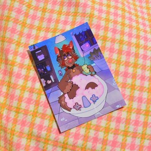 May include: A print featuring a cartoon character in a bathtub filled with pink bubbles. The character, a brown furry creature with red hair, is holding a cup. The background shows a window, a shelf with items, and a plant. The print is on a pink and yellow checkered surface.