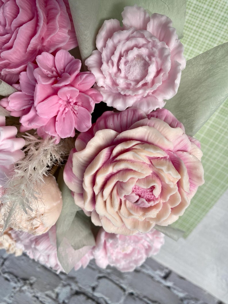 Puede incluir: Un ramo de flores de jab&oacute;n rosas y blancas dispuestas en un envoltorio de papel verde y blanco. Las flores est&aacute;n hechas para parecer peon&iacute;as y rosas.