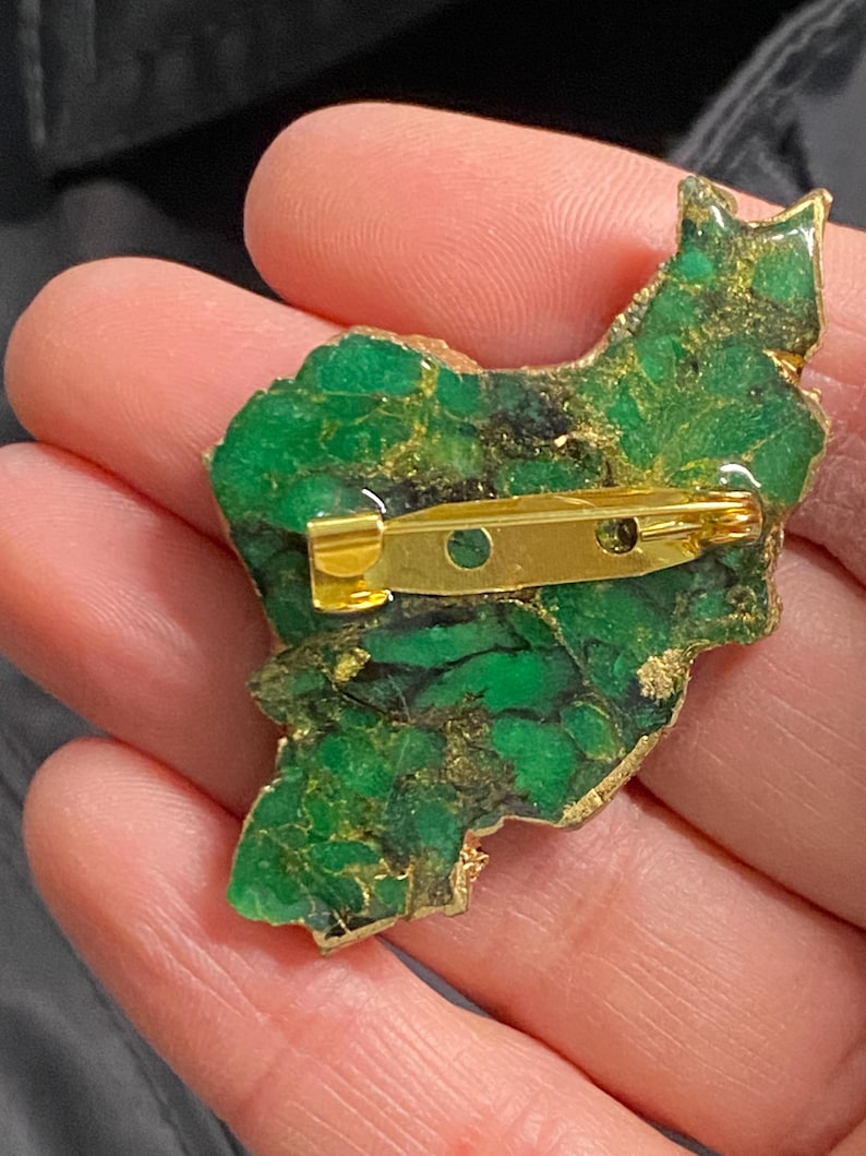 May include: A green and gold resin brooch shaped like the outline of a country. The brooch has a gold pin on the back.
