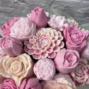 Puede incluir: Un ramo de flores de jab&oacute;n rosas y blancas, incluyendo rosas, peon&iacute;as, tulipanes y dalias. Las flores est&aacute;n dispuestas en un envoltorio de papel verde.