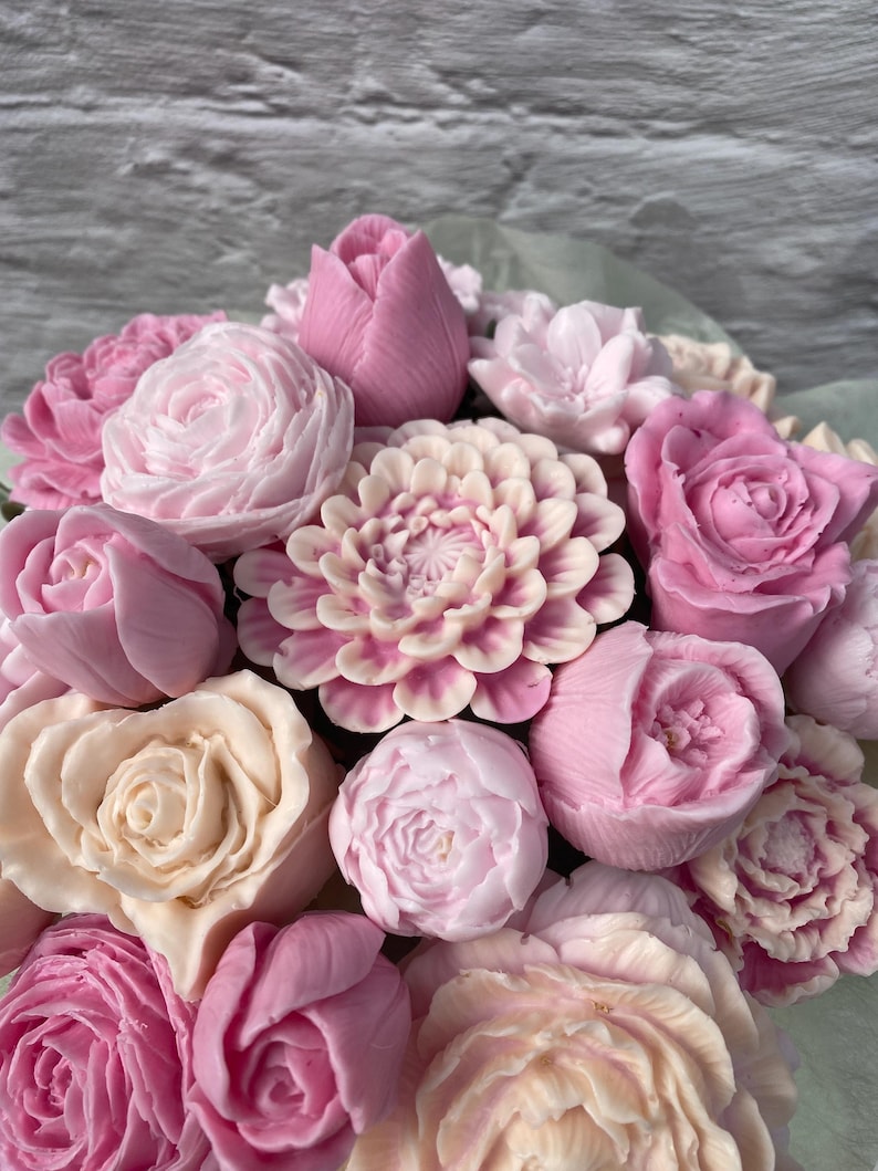 Puede incluir: Un ramo de flores de jab&oacute;n rosas y blancas, incluyendo rosas, peon&iacute;as, tulipanes y dalias. Las flores est&aacute;n dispuestas en un envoltorio de papel verde.