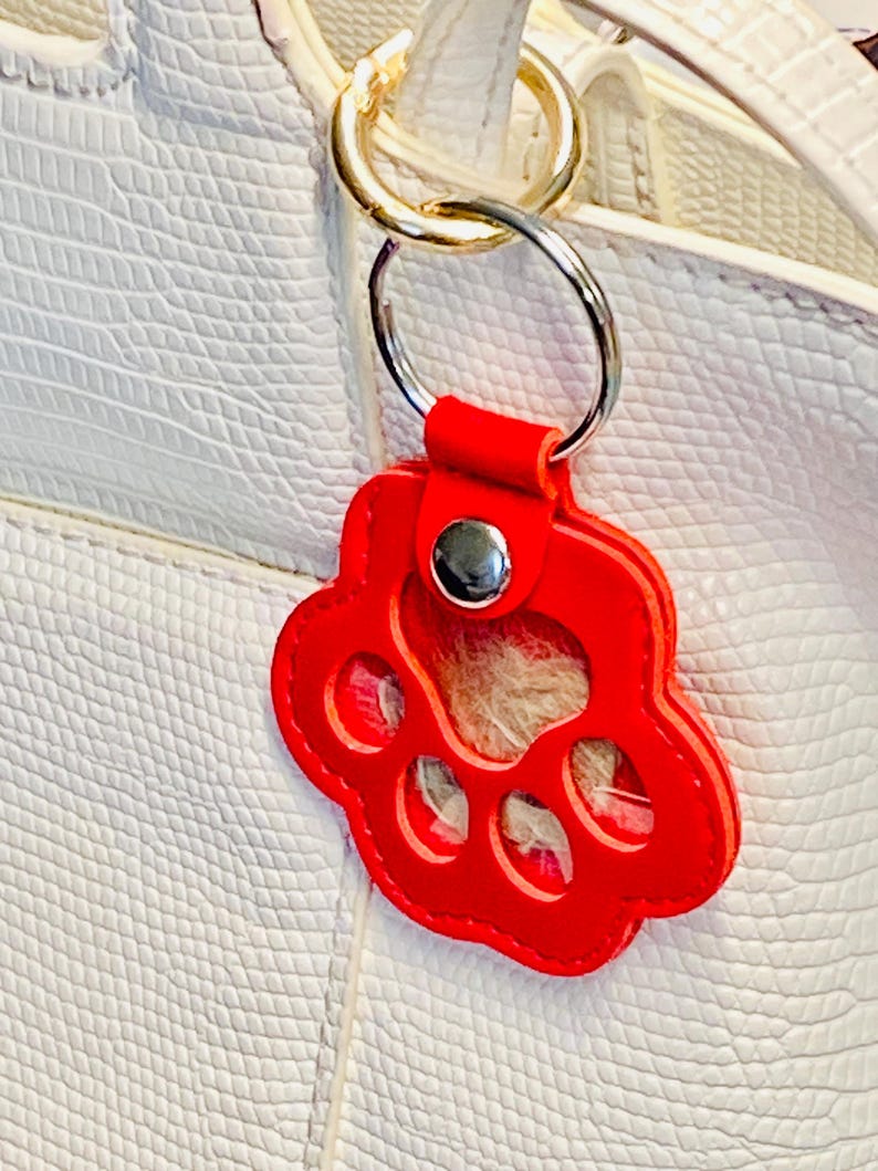 May include: Red leather paw print keychain with a clear plastic insert. The keychain is attached to a gold-colored metal ring.