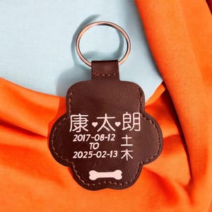 May include: Brown leather paw print keychain with a bone design. It has the text "健康" with a heart symbol on either side, followed by the dates "2017-08-12" and "2025-02-13" with the words "土" and "木" below the dates.