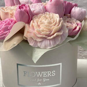 Puede incluir: Un ramo de flores de jab&oacute;n rosa y blanco dispuestas en una caja de regalo redonda blanca con una etiqueta plateada que dice "FLOWERS just for you".