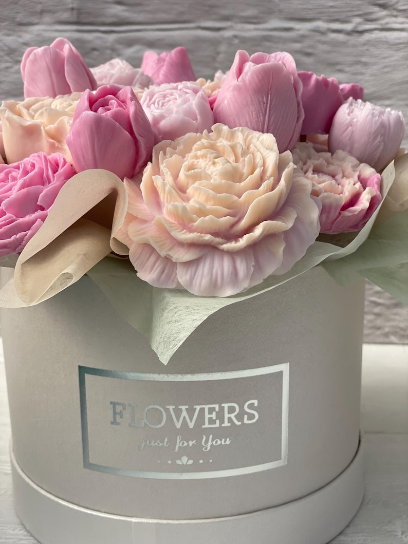 Puede incluir: Un ramo de flores de jab&oacute;n rosa y blanco dispuestas en una caja de regalo redonda blanca con una etiqueta plateada que dice "FLOWERS just for you".