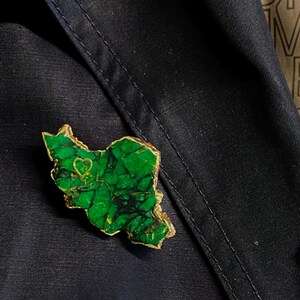 May include: A green and gold brooch shaped like a state with a small heart in the center.