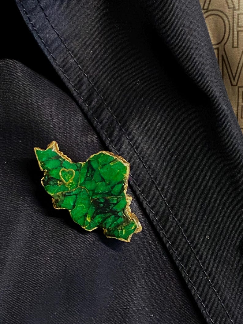 May include: A green and gold brooch shaped like a state with a small heart in the center.