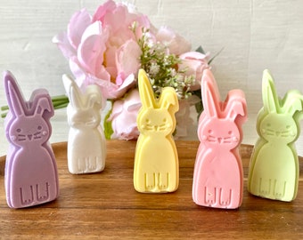 May include: Five pastel-colored bunny shaped soaps. The soaps are purple, white, yellow, pink, and green.