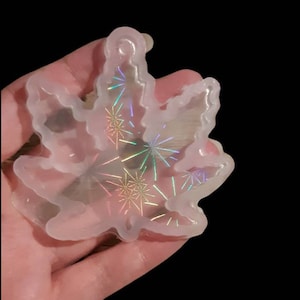 May include: A clear silicone mould shaped like a marijuana leaf with a holographic design inside. The mould is designed for making resin crafts.