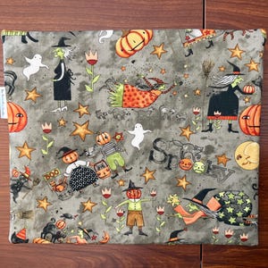 May include: A gray Halloween-themed fabric with a repeating pattern of witches, pumpkins, ghosts, stars, and the word "Spooky." The fabric features orange, black, white, and yellow accents, creating a festive and whimsical design.