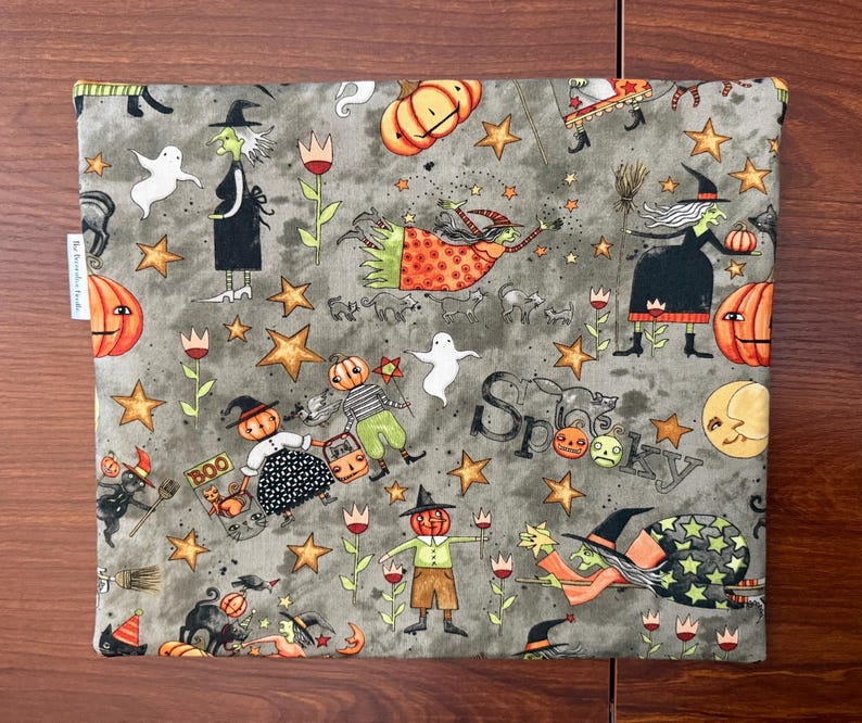 May include: A gray Halloween-themed fabric with a repeating pattern of witches, pumpkins, ghosts, stars, and the word "Spooky." The fabric features orange, black, white, and yellow accents, creating a festive and whimsical design.