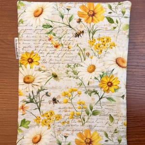 K&ouml;nnte beinhalten: Ein rechteckiger Stoffbeutel mit einem botanischen Druck aus wei&szlig;en und gelben G&auml;nsebl&uuml;mchen, kleinen gelben Wildblumen und Bienen vor einem Hintergrund aus verblasster Schreibschrift und hellbraunen Spritzern. Ein kleines wei&szlig;es Stoffetikett tr&auml;gt die Aufschrift The Decorative Needle.