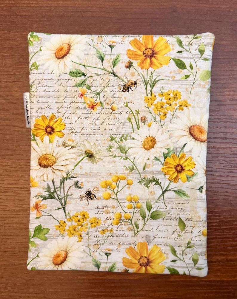 K&ouml;nnte beinhalten: Ein rechteckiger Stoffbeutel mit einem botanischen Druck aus wei&szlig;en und gelben G&auml;nsebl&uuml;mchen, kleinen gelben Wildblumen und Bienen vor einem Hintergrund aus verblasster Schreibschrift und hellbraunen Spritzern. Ein kleines wei&szlig;es Stoffetikett tr&auml;gt die Aufschrift The Decorative Needle.