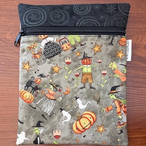 May include: A gray zippered pouch with a Halloween-themed pattern. The design features pumpkins, witches, ghosts, stars, and the word "BOO". The top section is black with a star and swirl pattern.