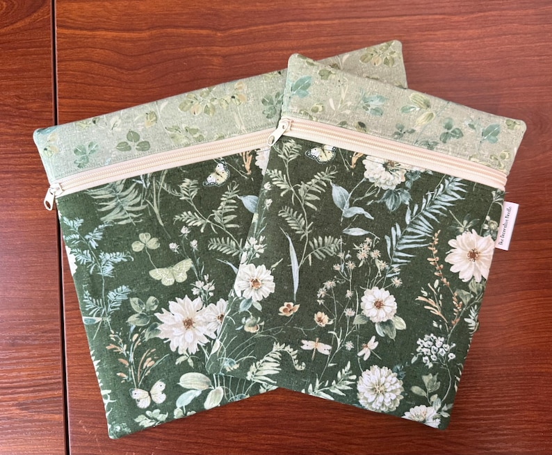 Pu&ograve; includere: Due pochette con cerniera con un motivo floreale verde scuro con fiori bianchi, farfalle e fogliame. La sezione superiore &egrave; verde chiaro con un design botanico simile. Le cerniere sono beige.