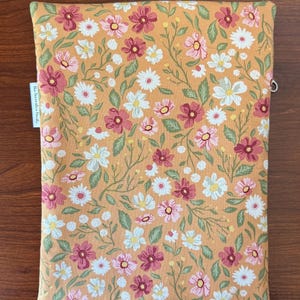 May include: A rectangular, floral-patterned case in shades of orange, pink, white, and green. The case features a repeating pattern of daisies and other flowers. The text "the decorative bundle" is printed on a white tag on the side.
