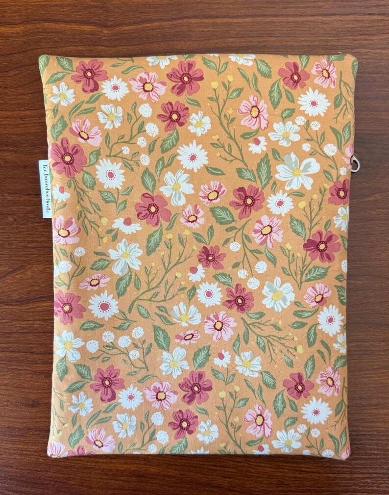 May include: A rectangular, floral-patterned case in shades of orange, pink, white, and green. The case features a repeating pattern of daisies and other flowers. The text "the decorative bundle" is printed on a white tag on the side.