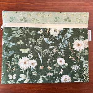 Pu&ograve; includere: Pochette rettangolare con cerniera con stampa botanica con fiori bianchi, farfalle e fogliame su sfondo verde scuro. La sezione superiore &egrave; verde chiaro con un motivo simile. Una cerniera color crema attraversa la parte superiore.