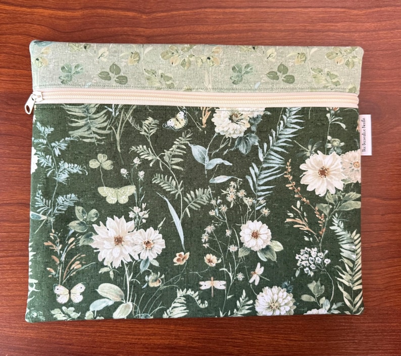 Pu&ograve; includere: Pochette rettangolare con cerniera con stampa botanica con fiori bianchi, farfalle e fogliame su sfondo verde scuro. La sezione superiore &egrave; verde chiaro con un motivo simile. Una cerniera color crema attraversa la parte superiore.