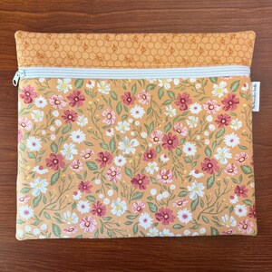 May include: A rectangular, floral-patterned pouch with a light blue zipper. The main body features a repeating pattern of pink, white, and burgundy flowers on a yellow background. The top section has a honeycomb pattern. The tag reads "The Decorative Beads".