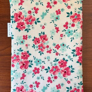 Puede incluir: Un art&iacute;culo de tela rectangular con un estampado floral. El dise&ntilde;o presenta un fondo blanco con flores rosas y turquesas y hojas verdes. El art&iacute;culo tiene una etiqueta que dice "The Decorative Needle."