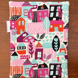 Puede incluir: Una bolsa de tela rectangular con un patr&oacute;n colorido de casas, &aacute;rboles y follaje en tonos rosa, naranja, negro y azul claro sobre un fondo blanco. Una peque&ntilde;a etiqueta de tela en el lateral muestra el texto The Decorative Needle.