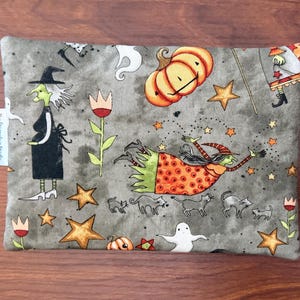May include: A rectangular, gray Halloween-themed pouch featuring illustrations of witches, pumpkins, stars, cats, and ghosts. The design includes a witch in a black dress and hat, and another flying with a wand. The pouch has a small white tag on the side.