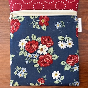 K&ouml;nnte beinhalten: Ein rechteckiger Rei&szlig;verschlussbeutel mit floralem Muster. Der Hauptteil ist marineblau mit roten Rosen, wei&szlig;en G&auml;nsebl&uuml;mchen und kleinen blauen Blumen. Der obere Teil ist rot mit wei&szlig;en Sternformen. Ein cremefarbener Rei&szlig;verschluss ist sichtbar.
