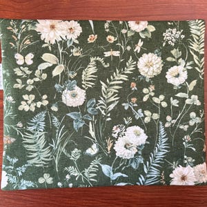 Pu&ograve; includere: Un tessuto rettangolare con un motivo floreale verde con fiori bianchi, farfalle e felci. Il tessuto ha uno sfondo verde scuro con un fitto motivo di elementi botanici. Una piccola etichetta bianca con testo &egrave; visibile sul lato sinistro.